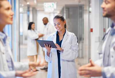 Lächelnde Ärztin in weißem Kittel steht auf dem Krankenhausflur mit einem Computer-Tablet in der Hand.